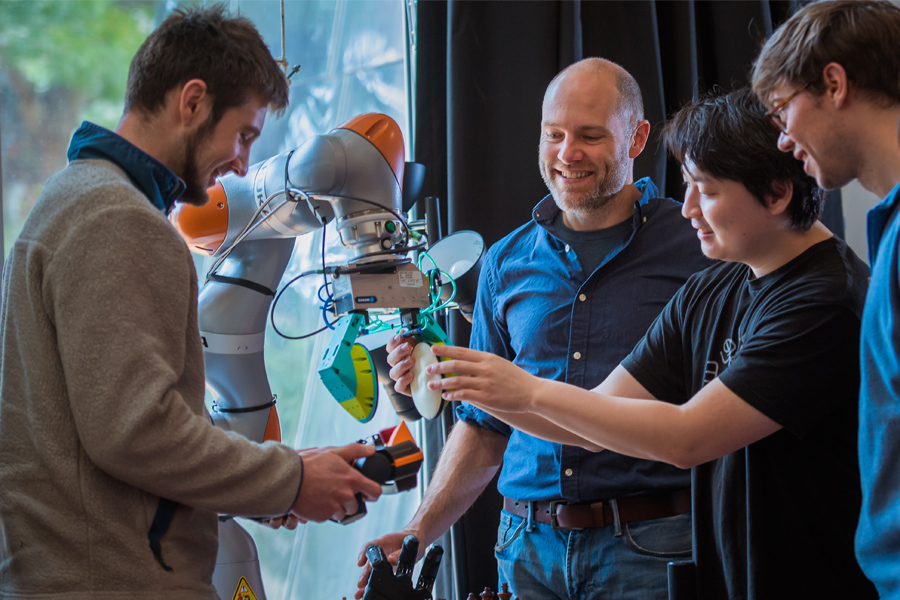 Photo of Professor Russ Tedrake examining robotic arm with students from 6.800