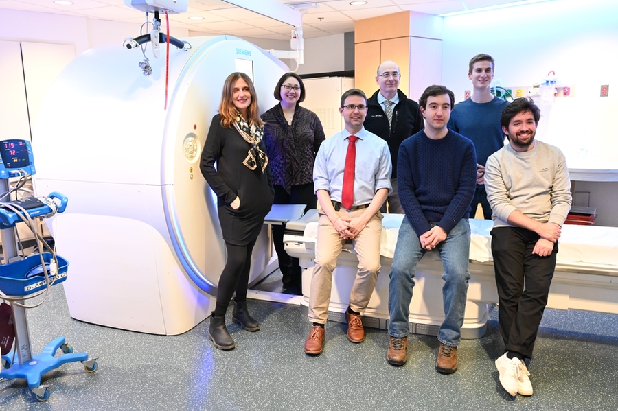 Photo of researchers posing in front of a CT scanner in two rows.