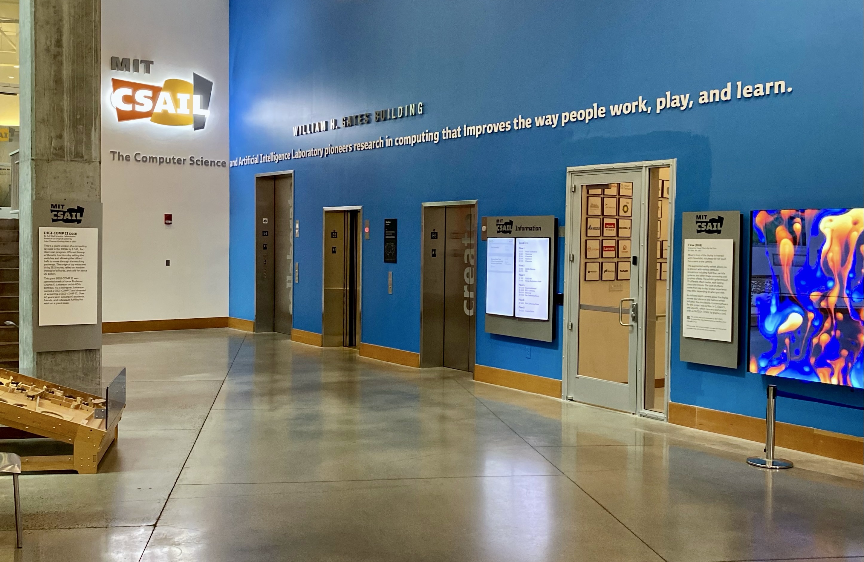 Interior photo of lobby in MIT Stata Center building, with MIT CSAIL logo signage, elevators, and a video installation titled "Flow"